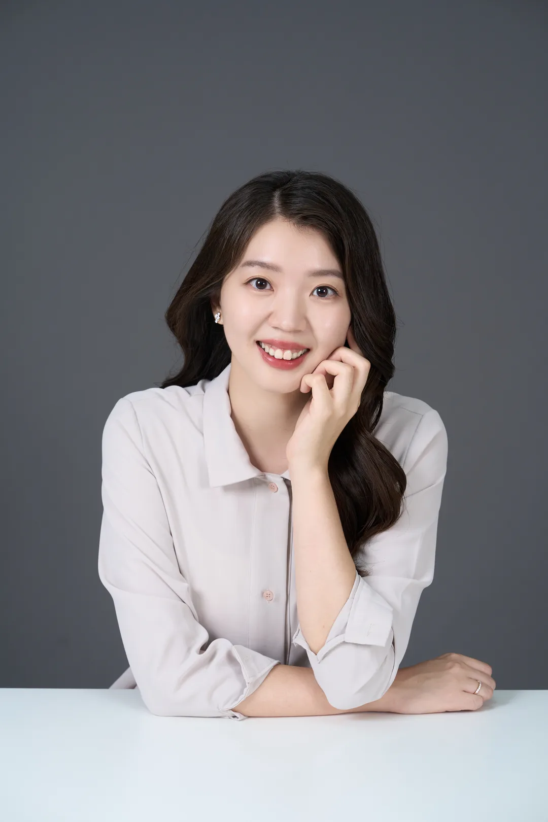 形象照作品：穿淺色襯衫、坐在白桌前托著臉微笑的女生